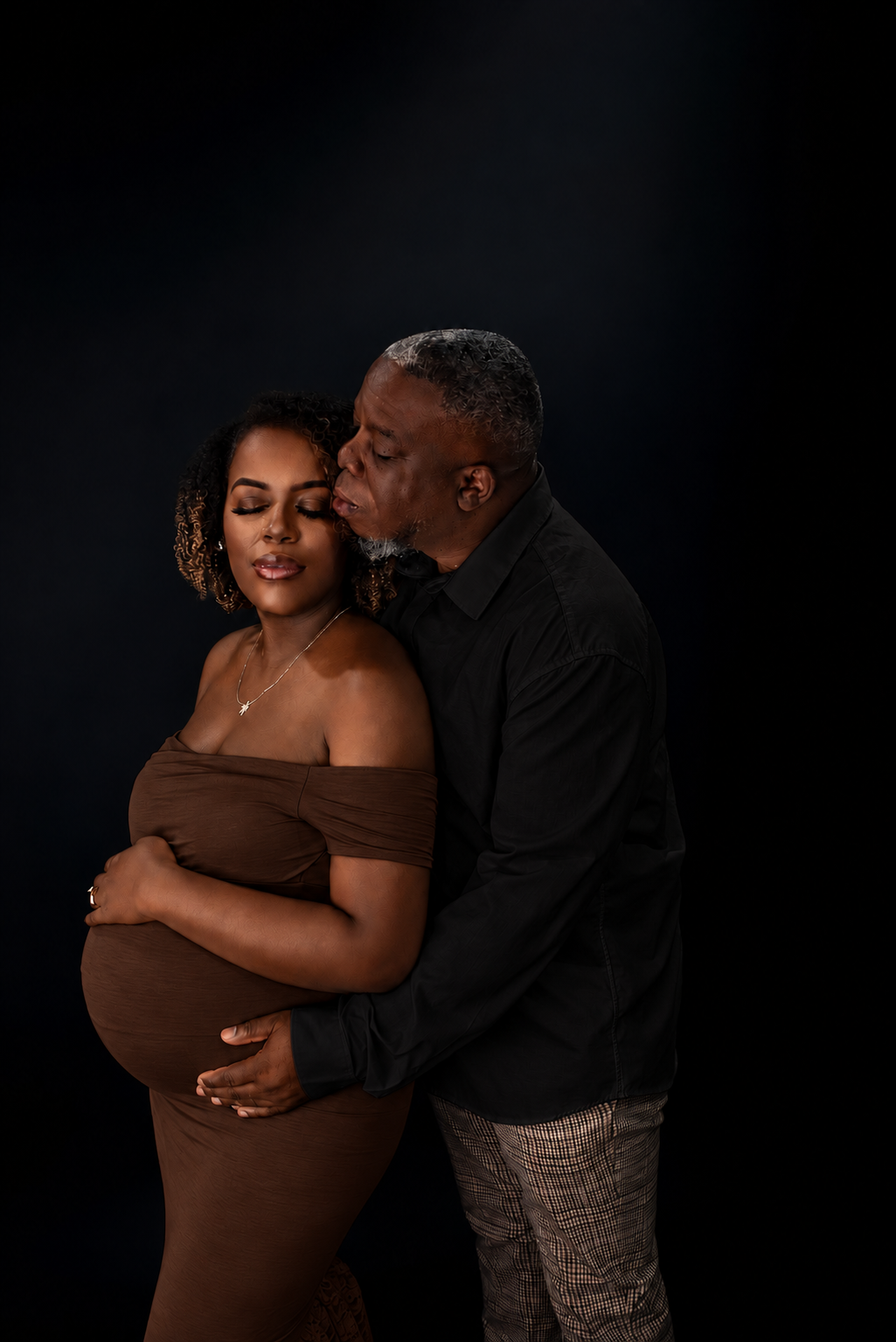 Expectant mother with her partner gathered close in warm low light, family maternity portrait
