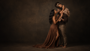 Family of three standing close together against a dark brown studio backdrop